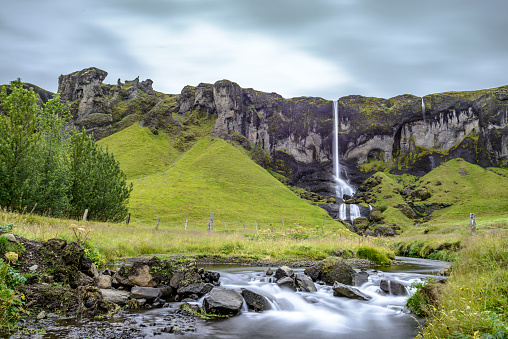 Long exposure image of smooth running water in a creek with a waterfall in the background in Iceland.