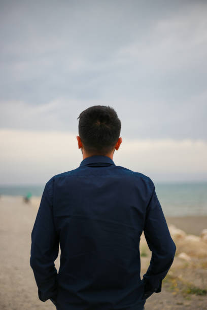 istock Unhappy man alone, looking at distant sea or seascape horizon. 1477135148