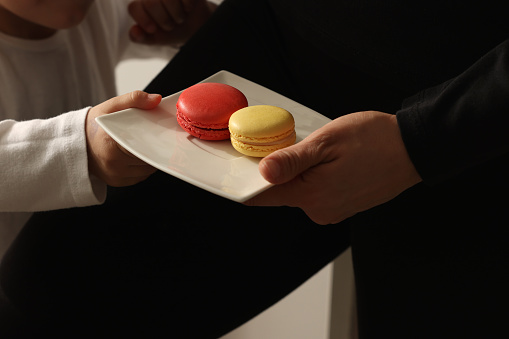 Woman holding coffee shares macarons with daughter