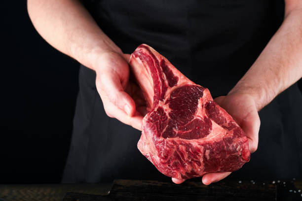 istock Chef cutting steak beef. Mans hands hold raw steak Tomahawk on rustic wooden cutting board on black background. Cooking, recipes and eating concept. Selective focus. 1477142337