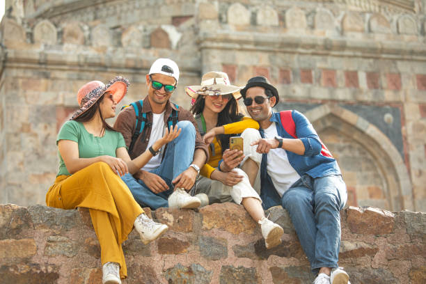 Group of cheerful friends spending leisure time and using phone during vacation at historic site
