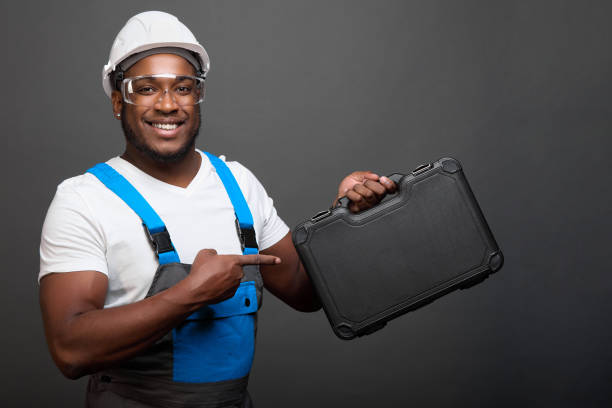 Cheerful African American man in robe and protective helmet demonstrates box with tools for auto mechanic. Strong black male auto mechanic by profession advertises professional tools in convenient box