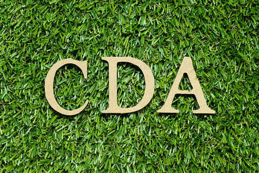 Wood alphabet letter in word CDA (Abbreviation of Confidential disclosure agreement) on green grass background