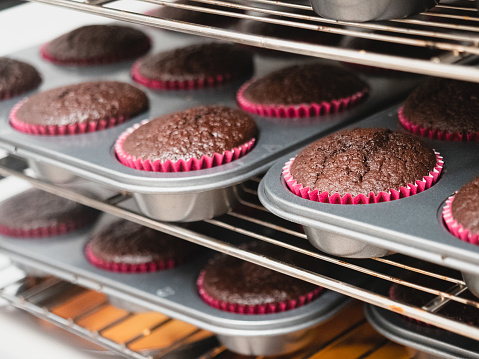 pastry chef baking a large group dark chocolate red velvet filled cupcakes in professional ventilated oven , small artisan production at caterer