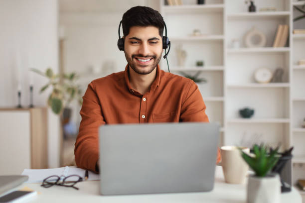 istock Arab man using laptop wearing headset sitting at desk 1477153693