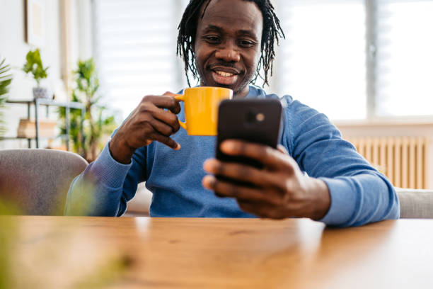 istock Young Man Sitting At The Kitchen Table Texting On The Phone And Drinking Coffee 1477155468