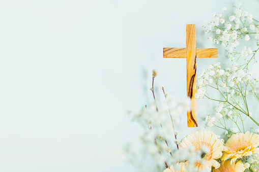 Wooden cross with spring flowers on blue background with copy space. Religion background. Religious church holidays. Christianity Feast, Easter, Palm Sunday, Christening, church wedding. Flat lay