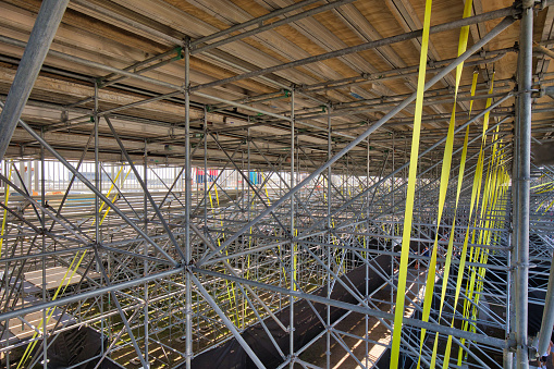 Underneath a large scaffolding and temporary grandstand showing a vast amount of pipes and straps.