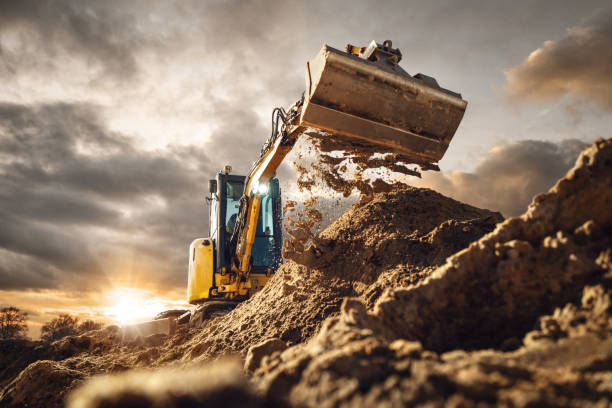 ドラマチックな空の前で土をすくう掘削機 - ショベルカー ストックフォトと画像