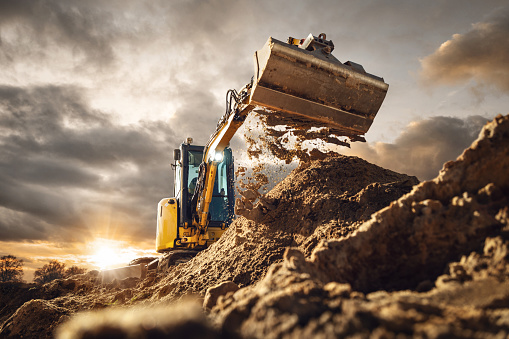 Excavator scooping dirt in front of a dramatic sky