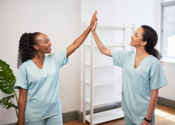 Two female doctors high five in clinic, wearing scrubs celebrate success stock photo