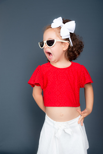 Beautiful happy little girl wearing sunglasses posing for photo. Isolated on gray background.