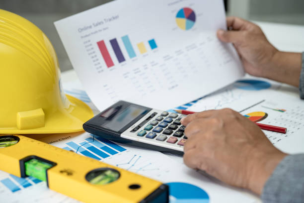 istock Asian engineer with architectural house plan project blueprint, graph and yellow helmet and engineering construction tools. 1477179132