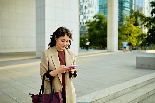 Three-quarter front view of Hispanic businesswoman leaving work at end of day and using portable device.