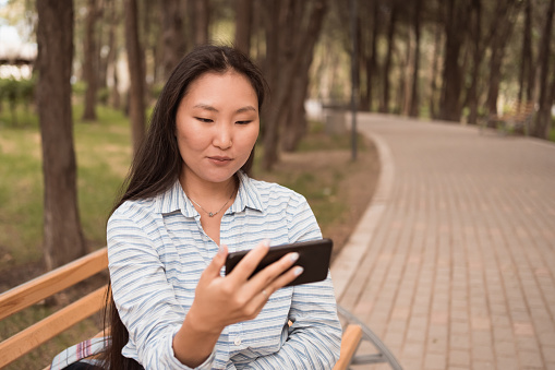 Close up portrait of young asian woman using smart phone for watching video call sitting in urban park