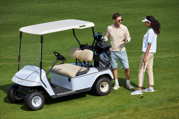 couple élégant debout près d’une voiturette de golf sur un terrain vert et bavardant au soleil - golf cart golf bag horizontal outdoors photos et images de collection