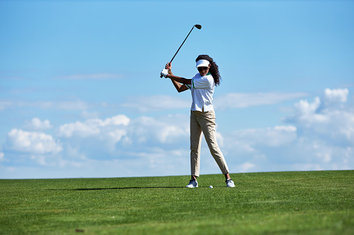 Minimal full length portrait of sporty young woman playing golf on green field against sky and swinging golf club with precision, copy space
