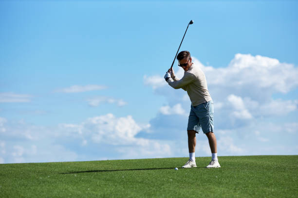 istock Active man swinging golf club on field against blue sky 1477183561