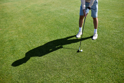 Low section of unrecognizable man playing golf on green grass and aiming for perfect shot, copy space