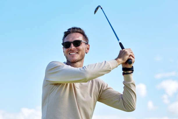 istock Smiling man playing golf and swinging golf club against blue sky 1477183652