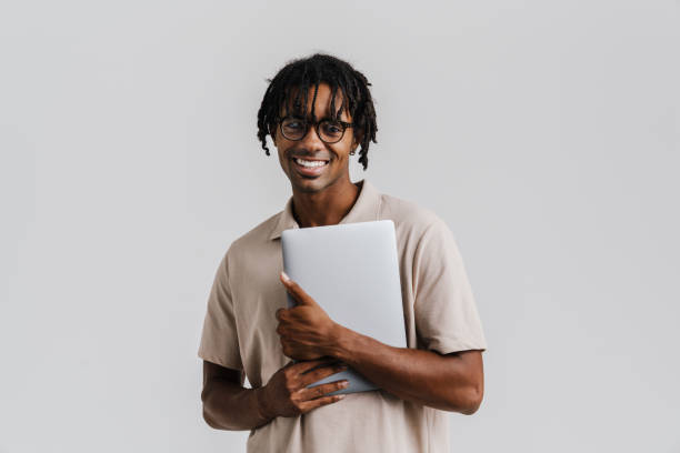 istock Excited young african man wearing glasses holding laptop while standing isolated 1477185939