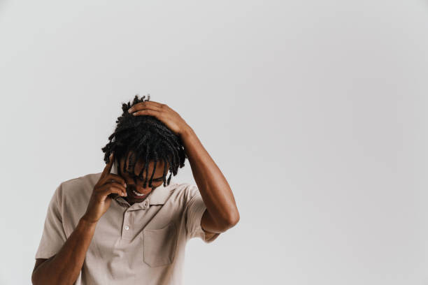 istock Smiling african man holding his head while talking on phone isolated over white background 1477185956