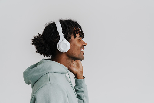 Profile of young african man smiling while listening music with headphones isolated over white background