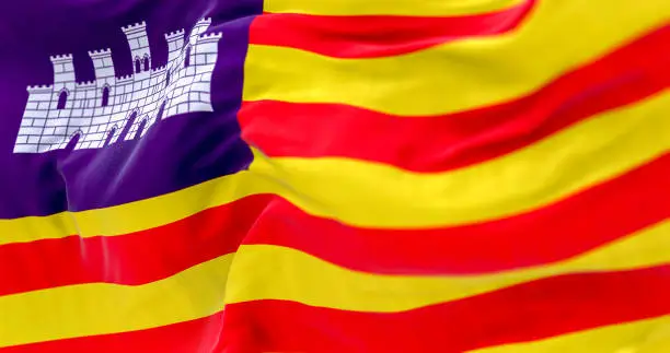 Detail of the Balearic Islands flag waving in the wind. Four red lines on yellow with white castle on purple canton. 3D illustration render. Selective focus. Close-up. Rippled Textile