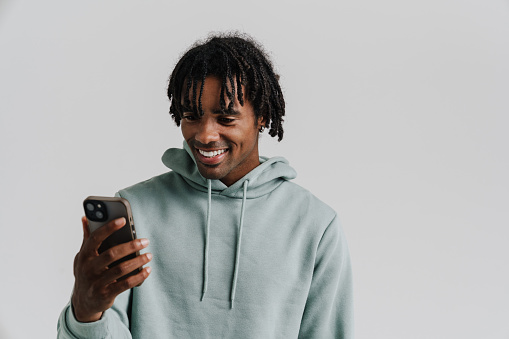 Black young man smiling while taking selfie photo on cellphone isolated over white background
