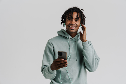 Excited young african man listening music with earphones using mobile phone isolated over white background