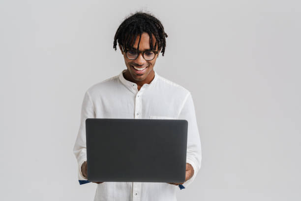 istock Excited african man in glasses using laptop while standing isolated 1477188072