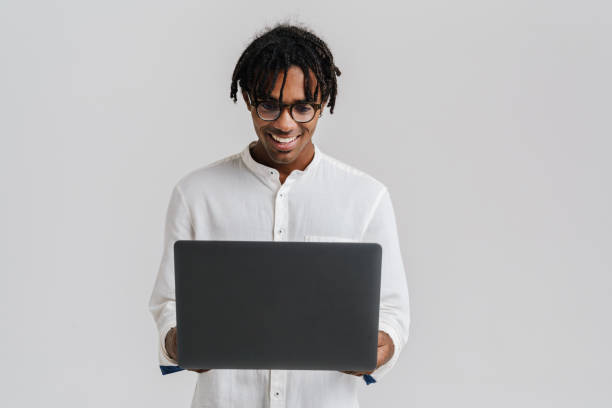 Excited african man in glasses using laptop while standing isolated stock photo