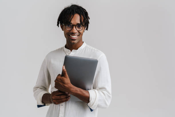 istock Excited african man in glasses holding laptop while standing isolated 1477188077