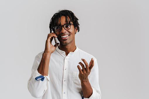 Black young man smiling while talking on mobile phone isolated over white background