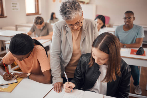 istock Help, classroom and professor with writing student in learning, mentorship and teaching at university, college or school. Knowledge, language and notes of a teacher with young woman for youth support 1477189241