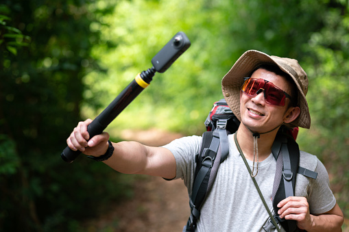 happy asian photographer travel and take photo with 360 digital camera and backpacker trail trekking in nature forest on high mountain, hobby activity in weekend