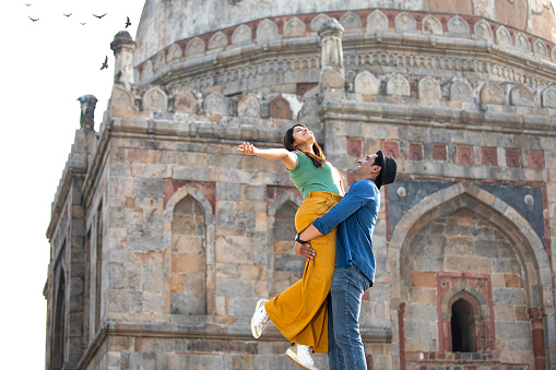 Happy loving man lifting up his girlfriend in the air during vacation at historic site
