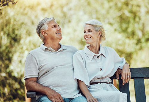 Love, retirement and couple on bench in park with smile, relax and bonding time in nature together. Romance, senior man and retired woman sitting in garden, happy people and romantic summer weekend.