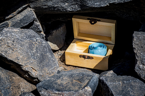 A thrilling geocaching adventure awaits as you uncover a hidden treasure chest nestled inside a small hole between black stones, revealing a blue geocaching logbook waiting to be signed.