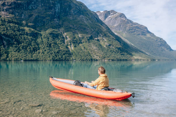 istock Man canoeing on a pristine lake through the mountains, the raft floats on the water surface, reflection 1477195515