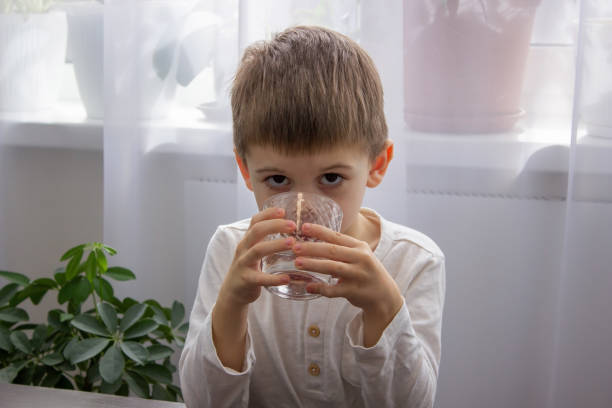 istock Cute little boy drinks water from a glass. 1477196992