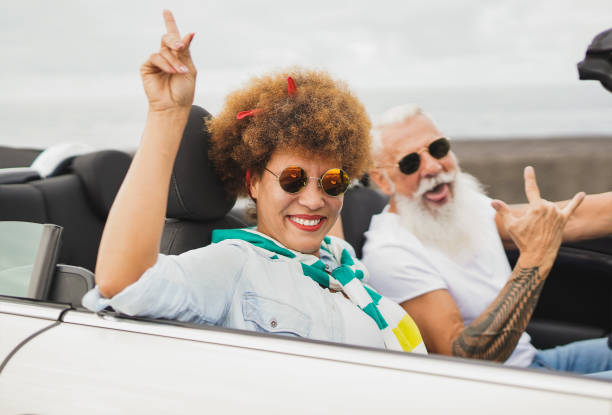 trendiges, multirassisches seniorenpaar, das spaß beim tanzen im cabriolet hat - ältere leute auf einem roadtrip im sommerurlaub mit dem cabriolet - outdoors car convertible wealth stock-fotos und bilder