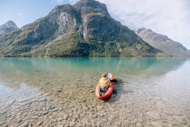 istock Man canoeing on a pristine lake through the mountains, the raft floats on the water surface, reflection 1477197435