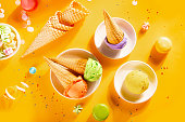 Various colorful ice cream scoops or balls with waffle cones on yellow background. Top view.