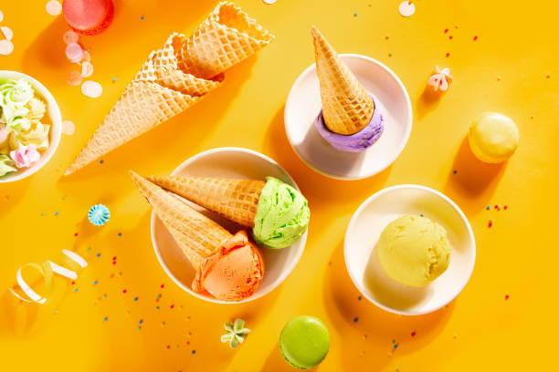 Various colorful ice cream scoops or balls with waffle cones on yellow background. Top view. stock photo
