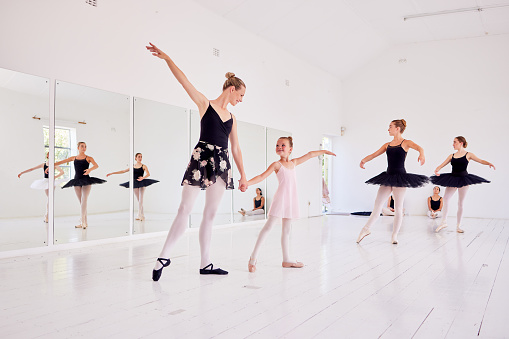 Ballet instructor or teacher teaching a young dancer in a class or dance studio preparing her for a performance. Young little girl learning to be a ballerina getting training for a coach