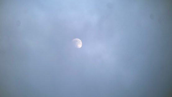 A moon partially visible during the day, mostly covered by thick dark cloud.