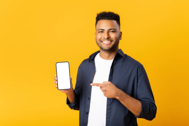 istock Happy excited young indian man looking at camera pointing finger at empty phone screen 1477205459