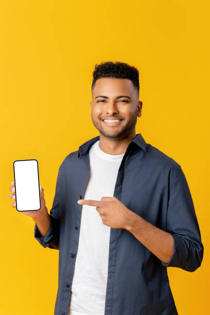 istock Positive indian man with pointing finger at smartphone with white empty display, bragging with application 1477205467