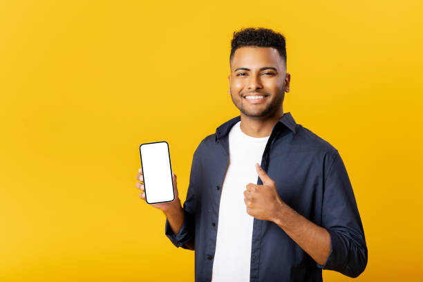 istock Happy young indian man looking at camera, holding smartphone with empty phone screen and showing thumb up in sign of approving, advertising new promotion 1477205505